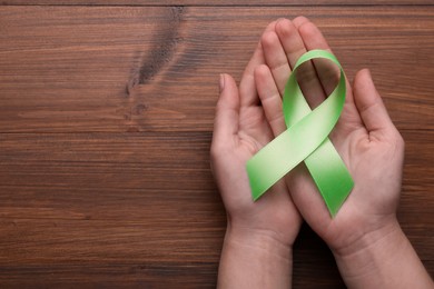 Photo of World Mental Health Day. Woman holding green ribbon on wooden background, top view with space for text