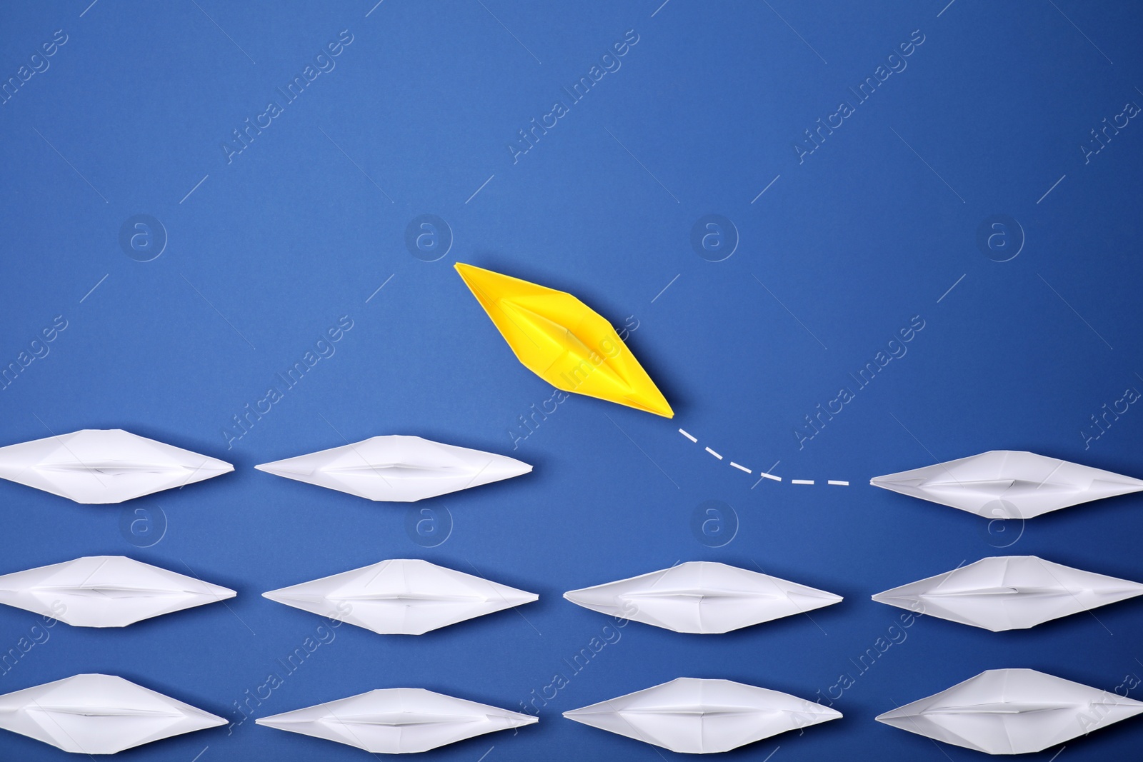 Photo of Yellow paper boat floating away from others on blue background, flat lay with space for text. Uniqueness concept