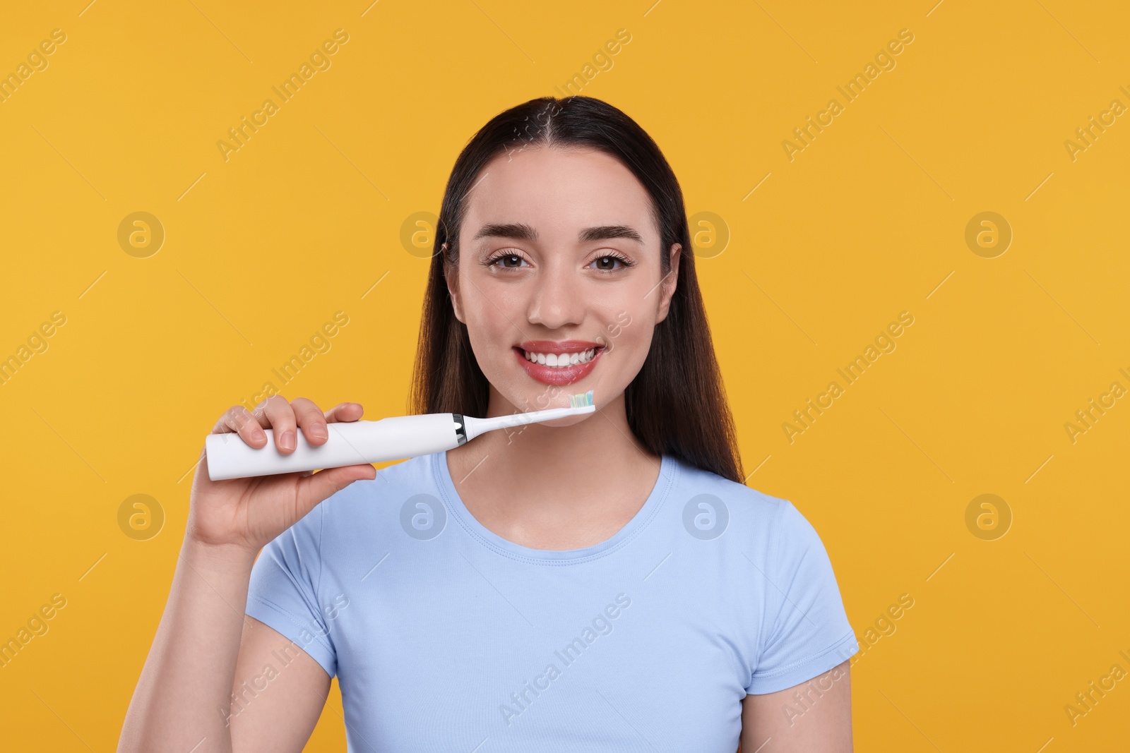 Photo of Happy young woman holding electric toothbrush on yellow background