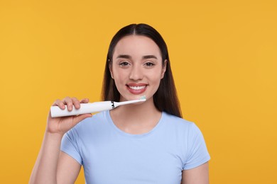 Happy young woman holding electric toothbrush on yellow background