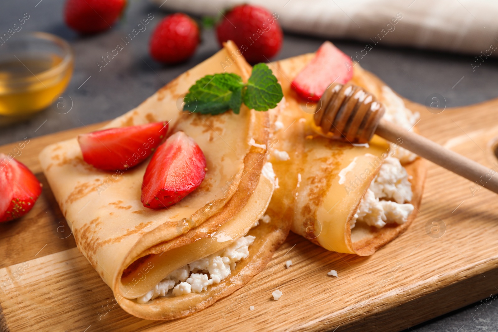 Photo of Delicious thin pancakes with strawberries, cottage cheese and honey on wooden board, closeup