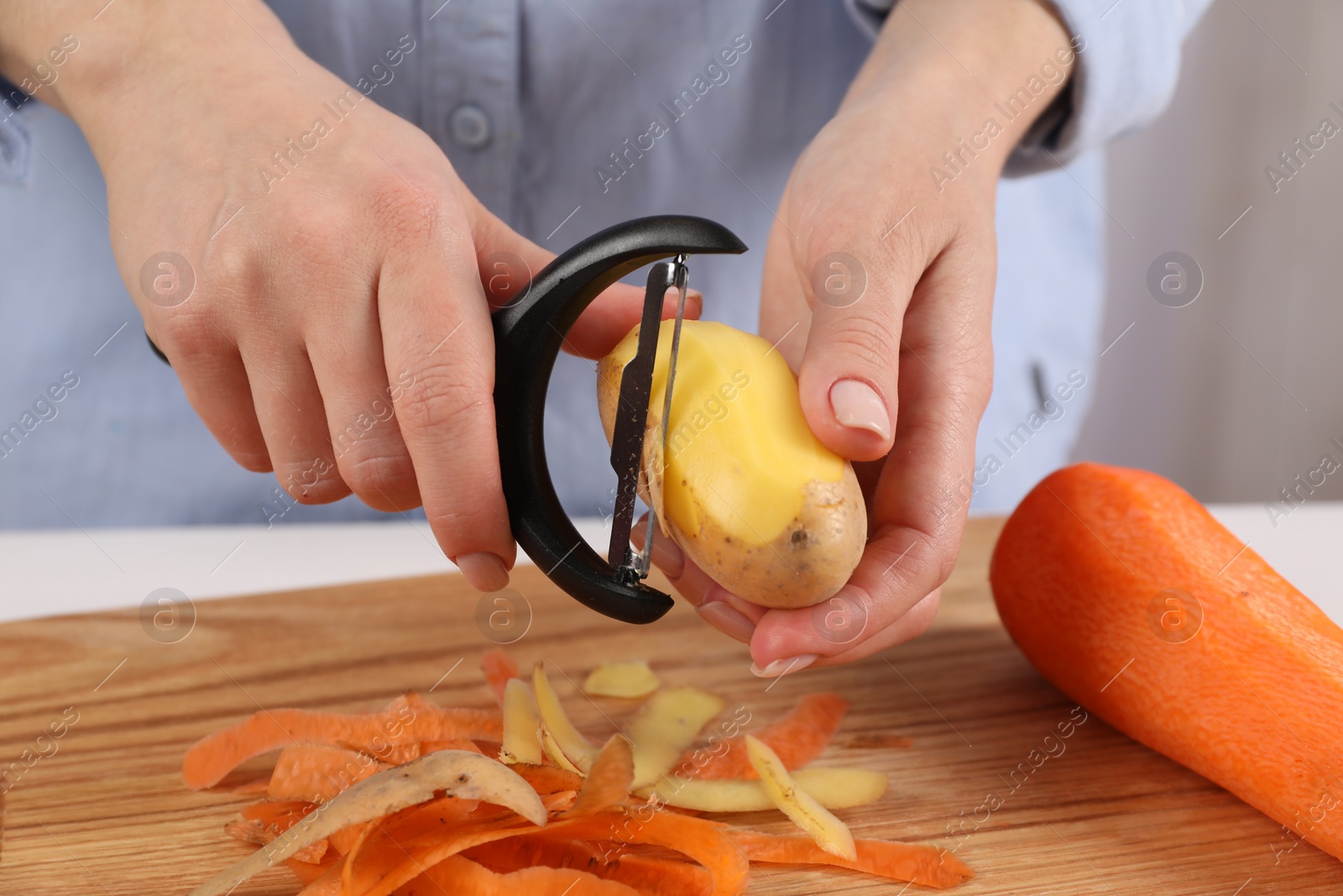 Photo of Woman peeling fresh potato at table indoors, closeup