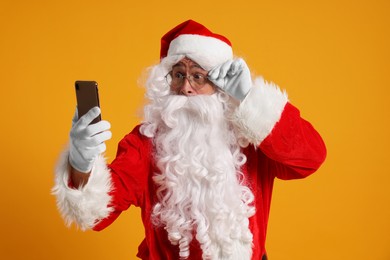 Photo of Merry Christmas. Santa Claus using smartphone on orange background