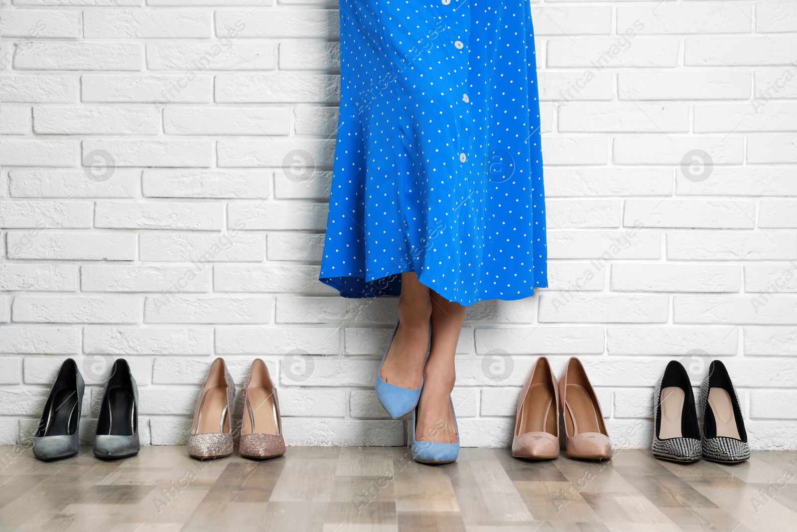 Photo of Woman trying on different shoes near white brick wall, closeup