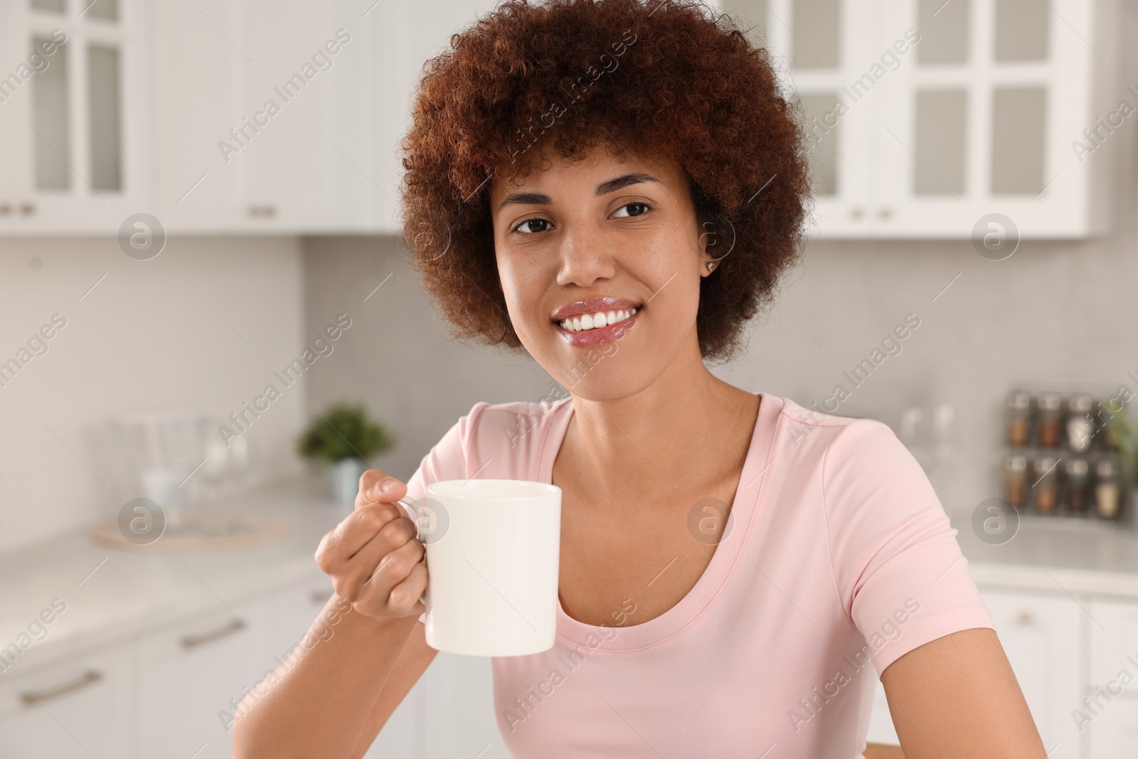 Photo of Happy young woman with cup of drink in kitchen