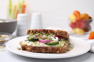 Tasty vegan sandwich with cucumber, onion, hummus and pumpkin seeds on light grey table, closeup