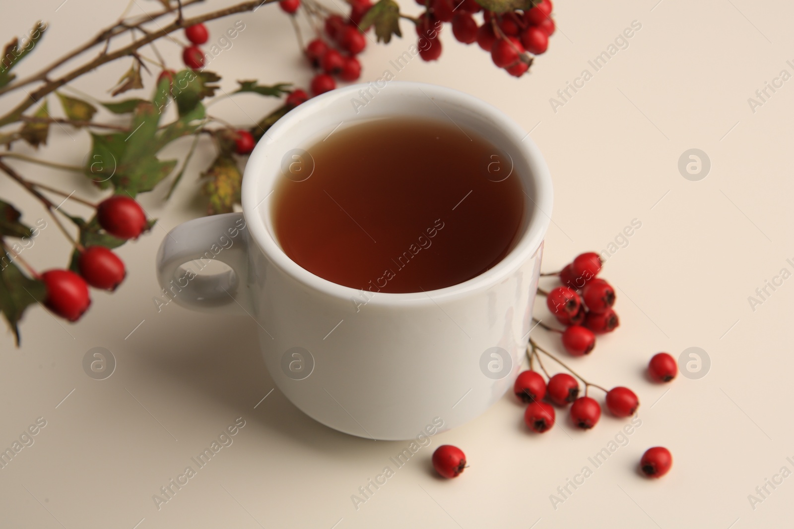 Photo of Aromatic hawthorn tea in cup and berries on beige table, closeup