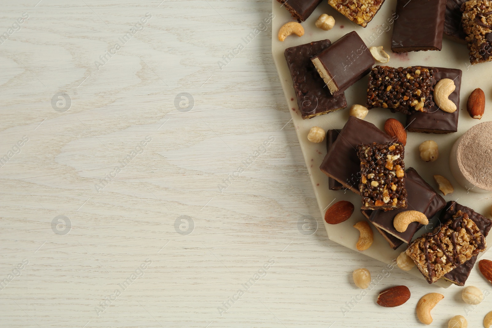 Photo of Different tasty energy bars, protein powder and nuts on white wooden table, flat lay. Space for text