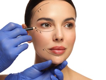 Woman preparing for cosmetic surgery, white background. Doctor drawing markings on her face, closeup