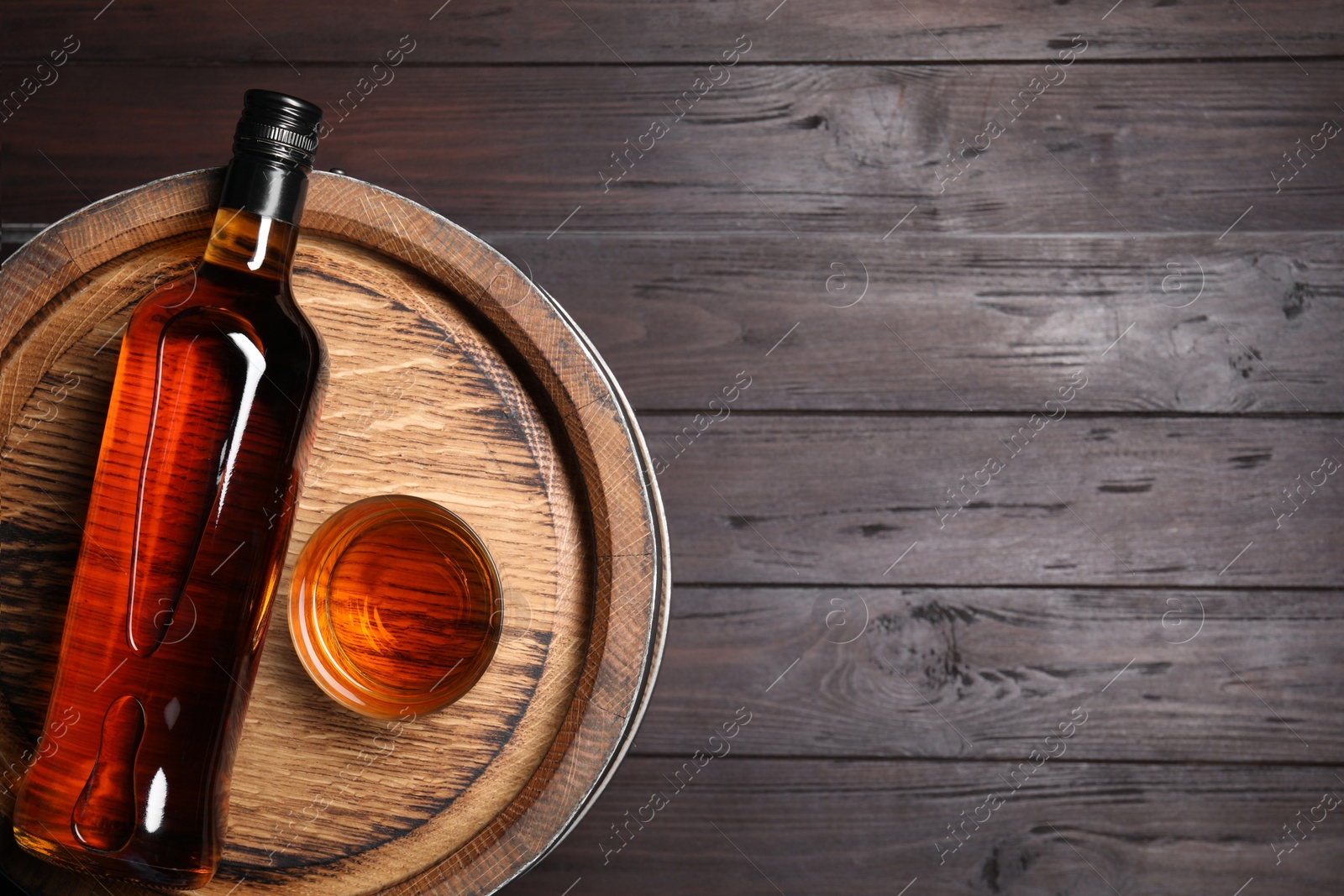 Photo of Barrel, bottle and glass of tasty whiskey on wooden table, top view. Space for text