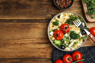 Photo of Bowl of delicious pasta with tomatoes, broccoli and cheese on wooden table, flat lay. Space for text