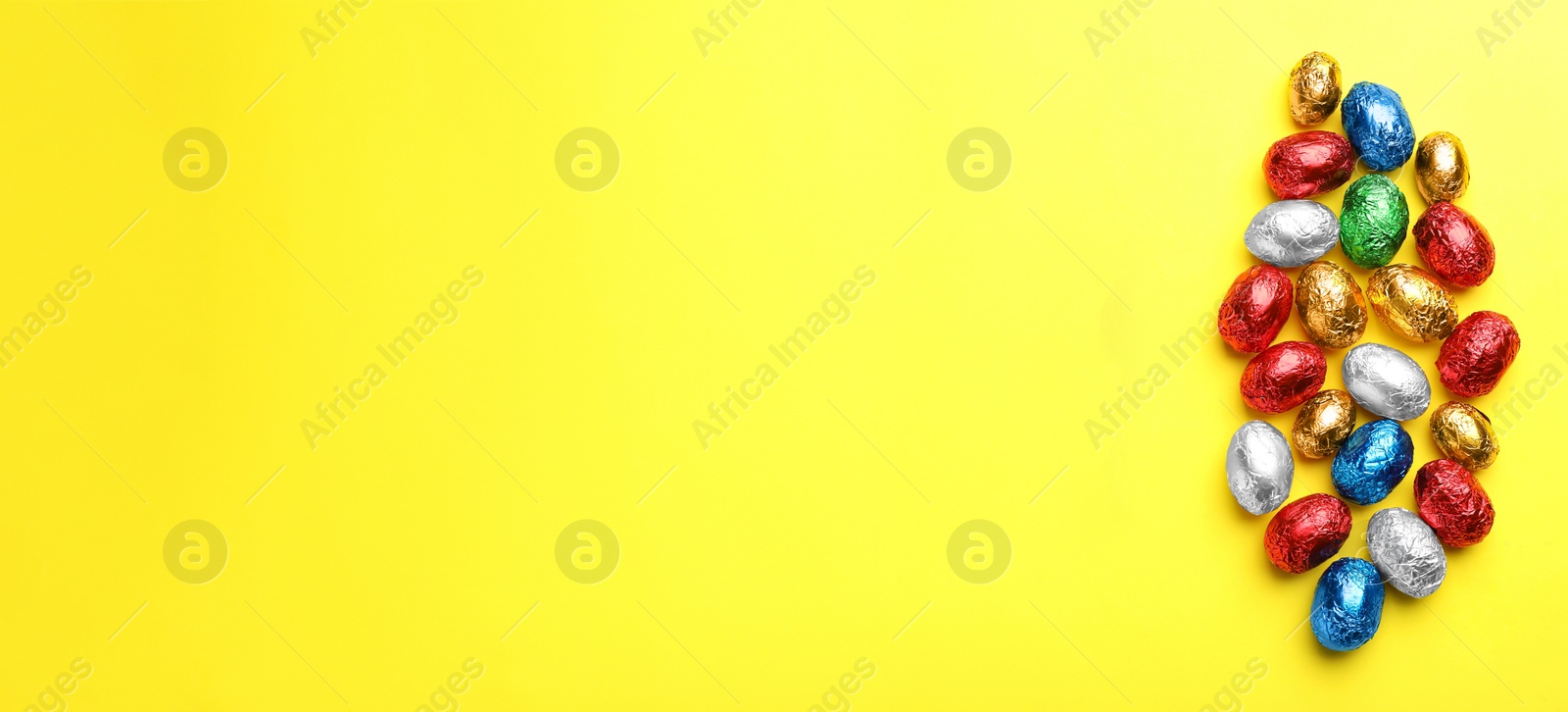 Photo of Chocolate eggs wrapped in colorful foil on yellow background, flat lay. Space for text