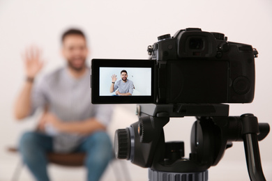 Photo of Young blogger recording video indoors, focus on camera screen