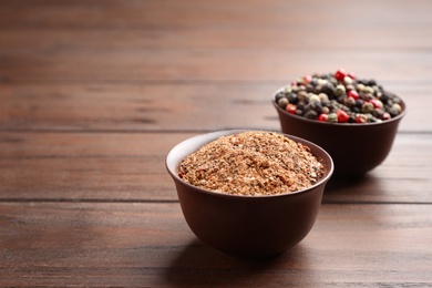 Photo of Bowls with powdered pepper and corns on wooden table, space for text