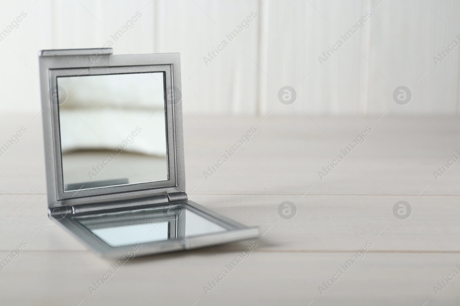 Photo of Stylish cosmetic pocket mirror on white wooden table. Space for text