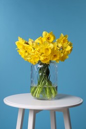 Beautiful daffodils in vase on white table against light blue background