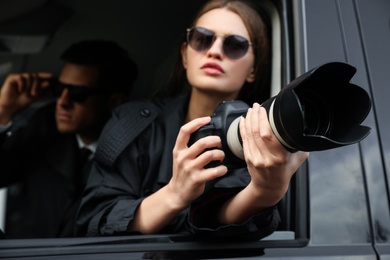 Photo of Private detectives with modern camera spying from car, focus on lens
