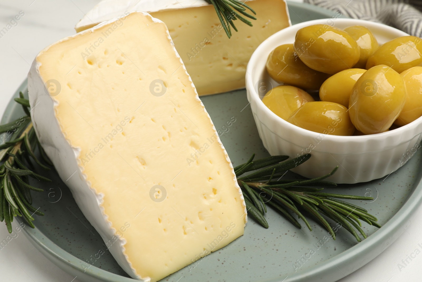 Photo of Plate with pieces of tasty camembert cheese, olives and rosemary on white table, closeup