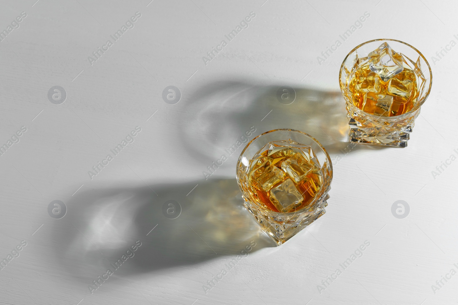 Photo of Whiskey with ice cubes in glasses on white table, above view. Space for text