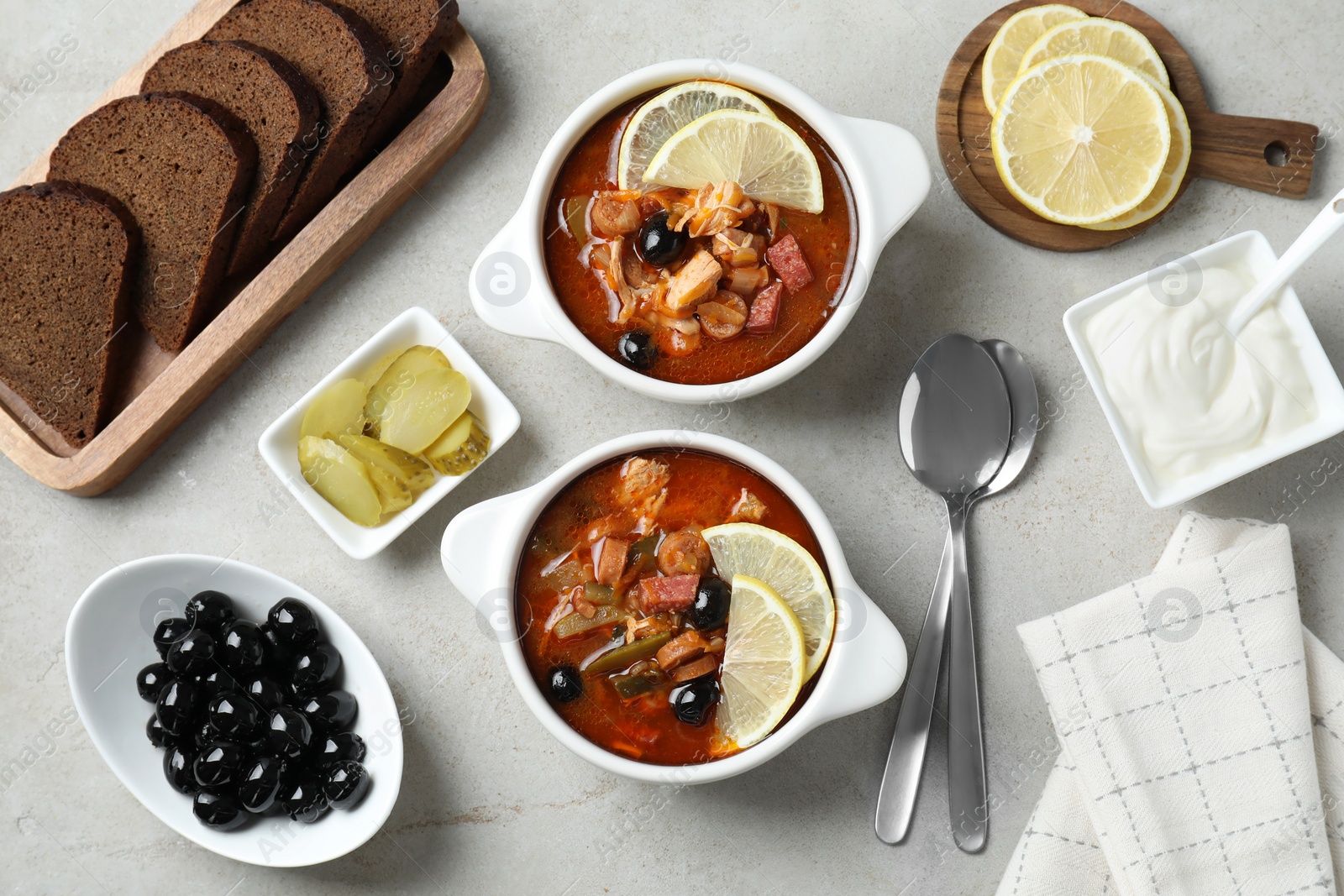 Photo of Meat solyanka soup with sausages, olives and vegetables served on white textured table, flat lay