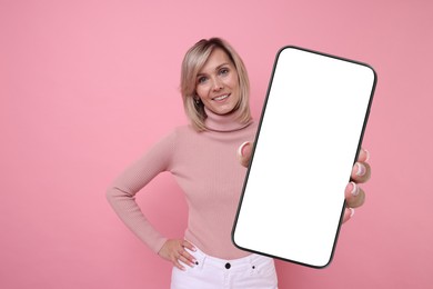 Happy woman showing mobile phone with blank screen on pink background. Mockup for design