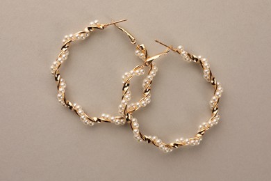 Elegant earrings with pearls on beige background, top view