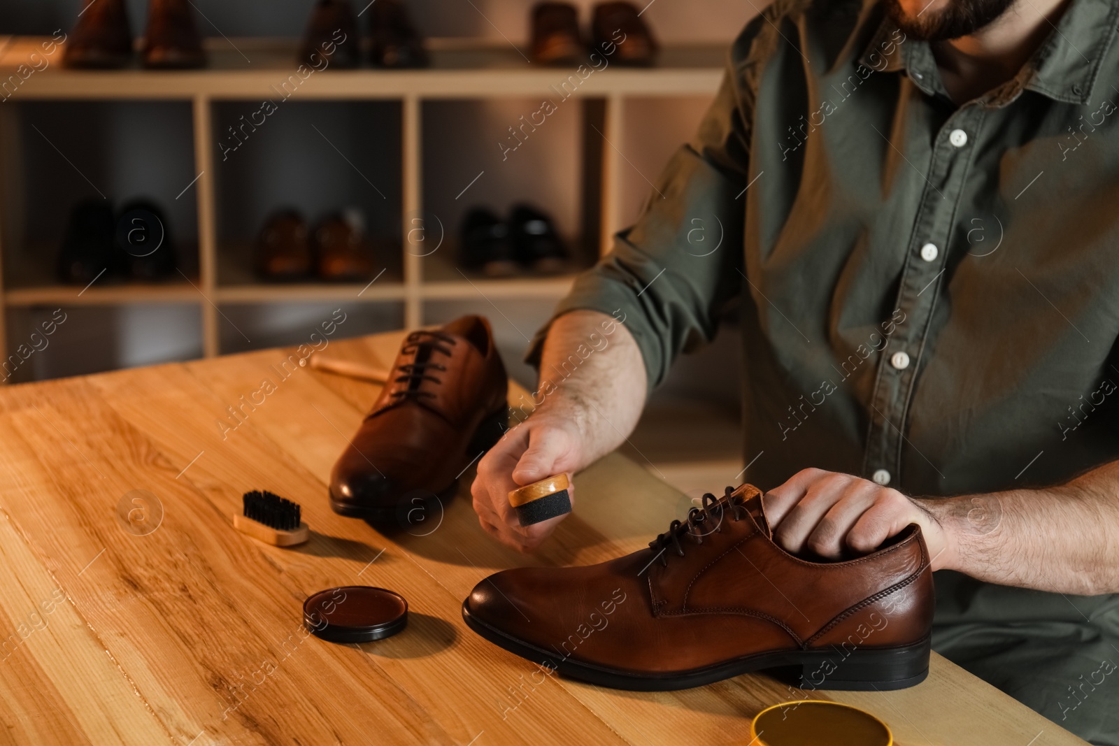 Photo of Man taking professional care of brown leather shoes in workshop, closeup