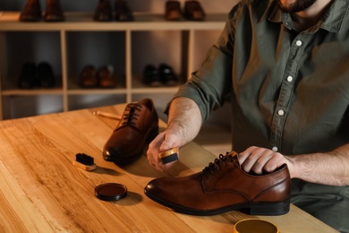 Man taking professional care of brown leather shoes in workshop, closeup