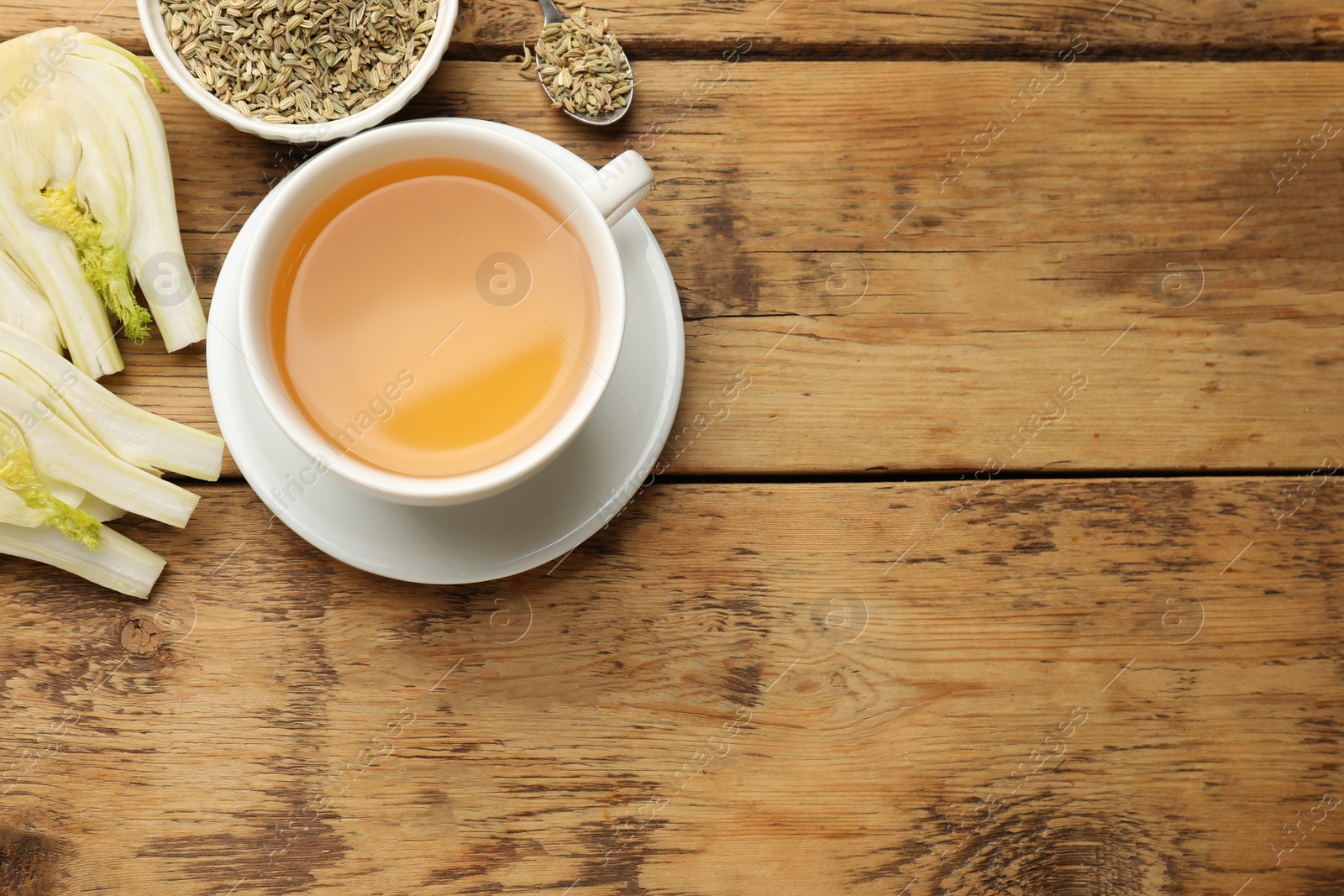 Photo of Fennel tea in cup, seeds and fresh vegetable on wooden table, flat lay. Space for text