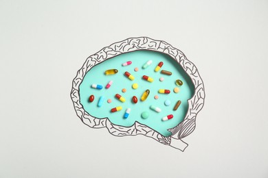 Photo of Pills on turquoise background, top view through paper with brain shaped hole and drawing