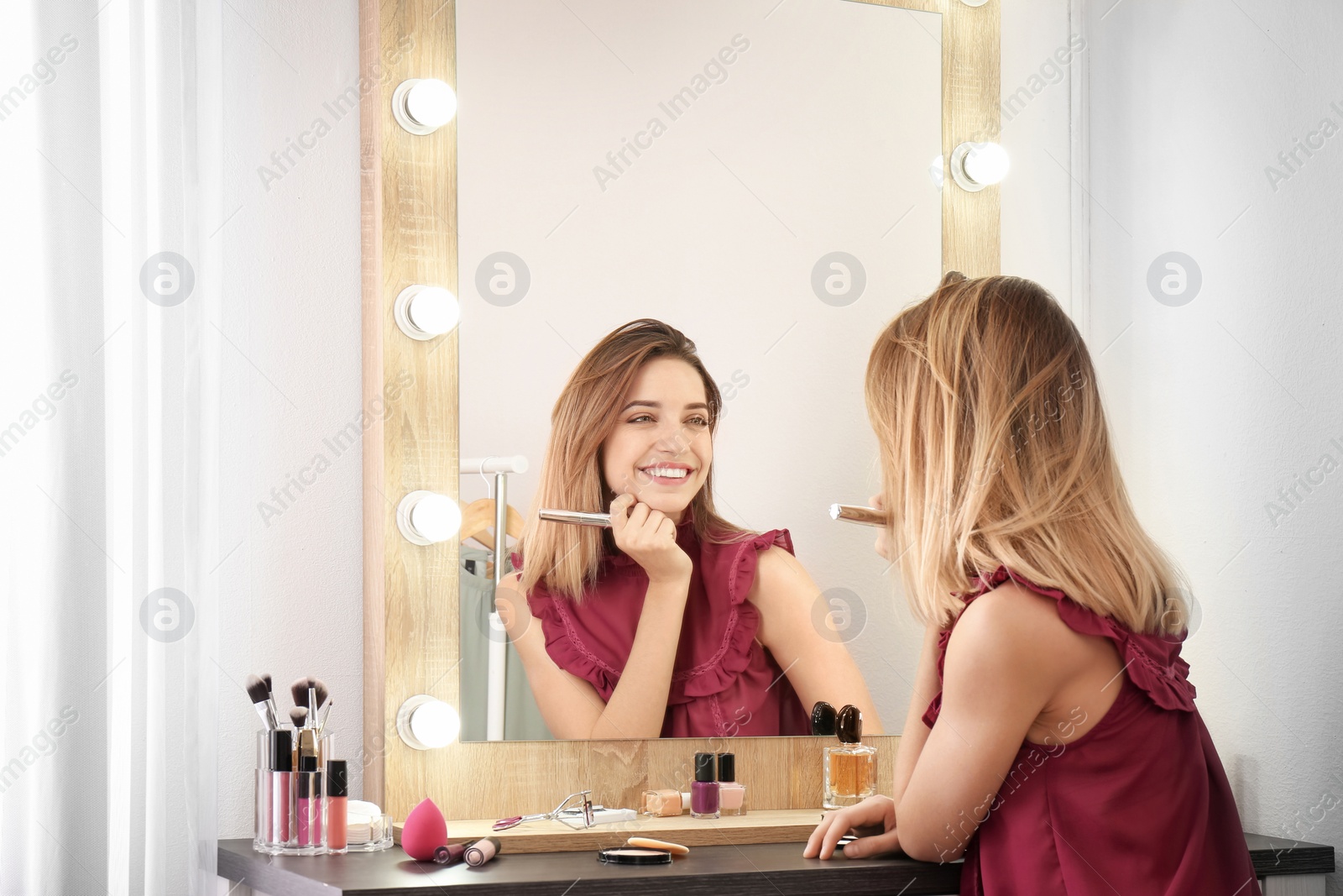 Photo of Woman applying makeup near mirror with light bulbs in dressing room