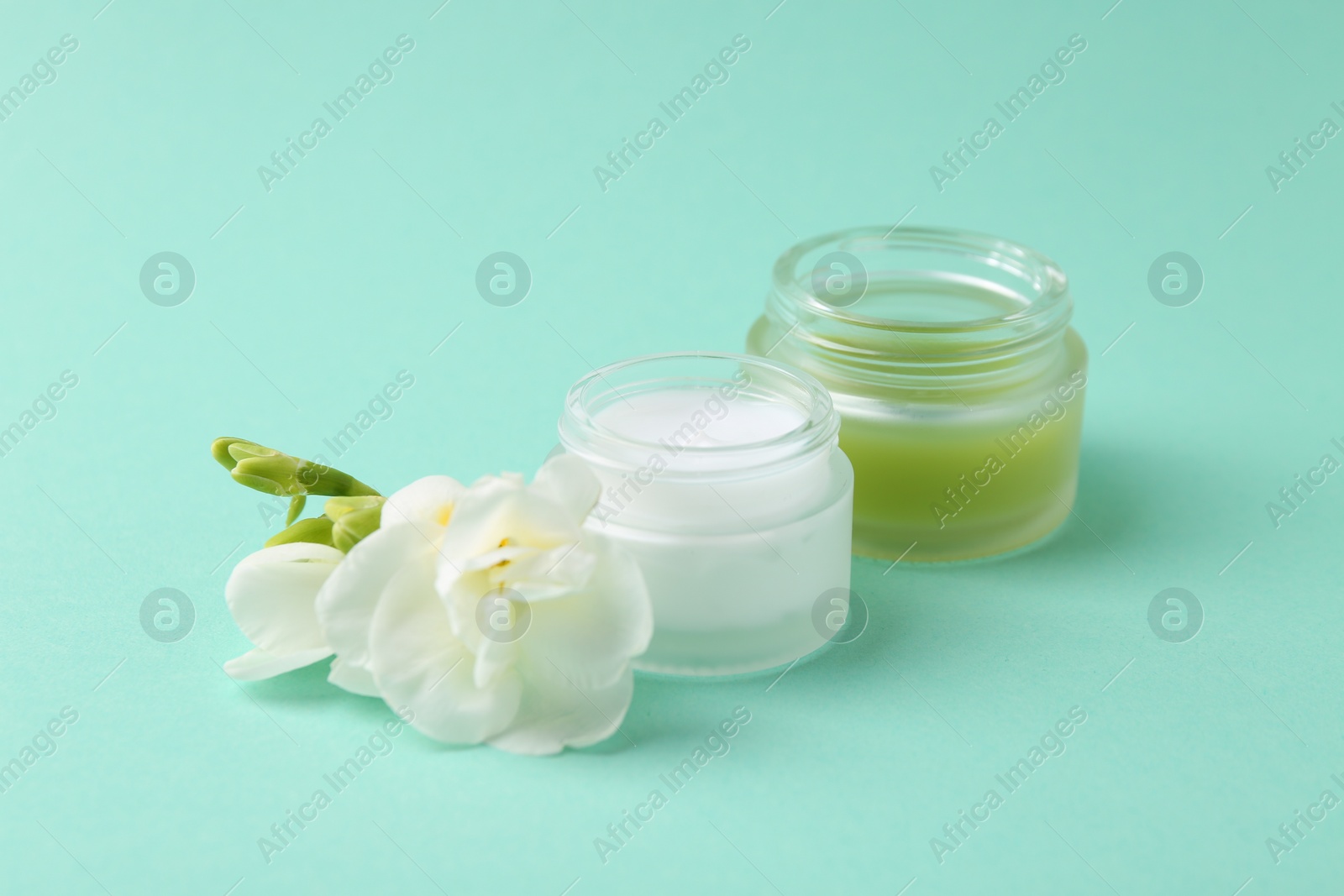 Photo of Moisturizing cream in open jars and freesia flower on turquoise background. Body care product