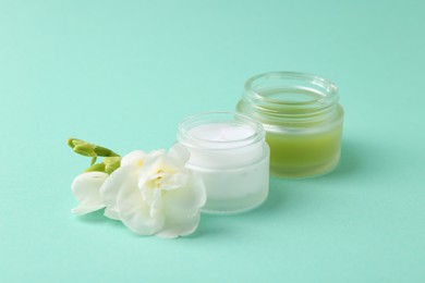 Photo of Moisturizing cream in open jars and freesia flower on turquoise background. Body care product