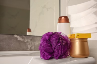 Photo of Purple shower puff and cosmetic products on sink in bathroom, space for text