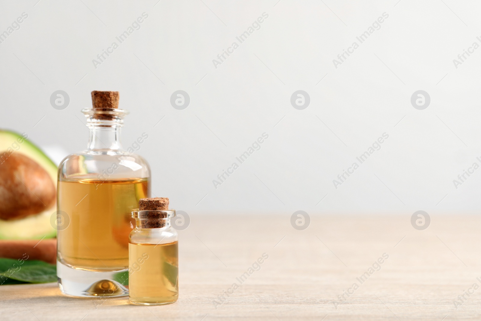 Photo of Bottles of essential oil and fresh avocado on light wooden table, space for text