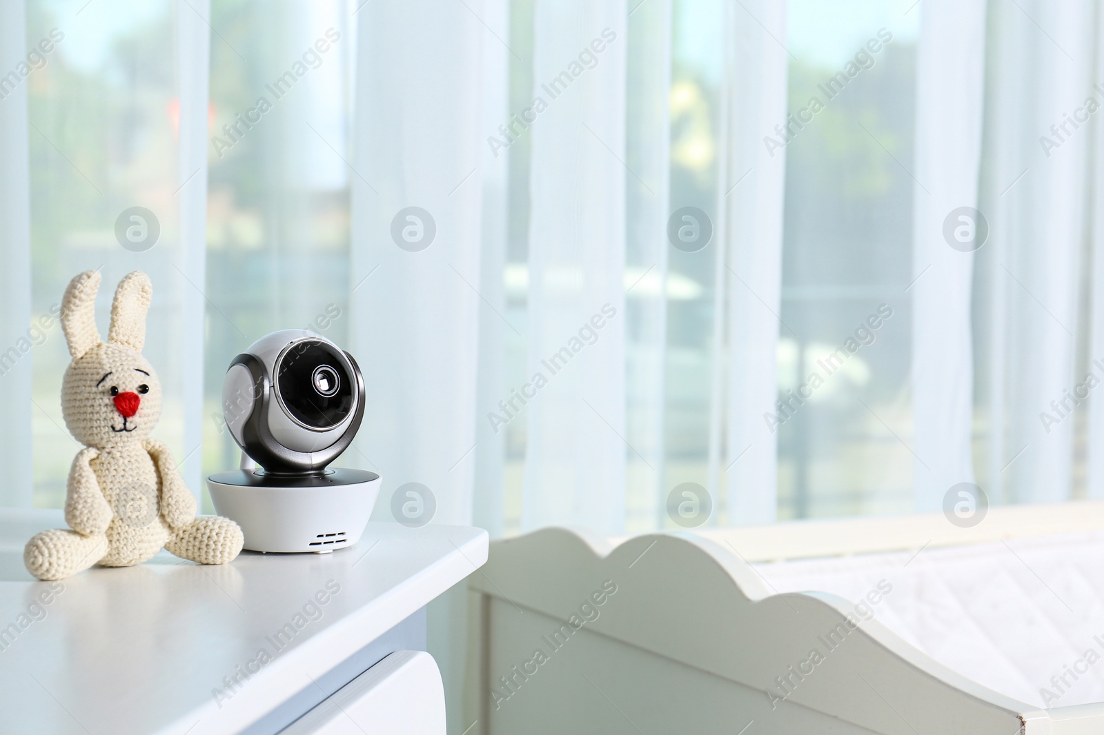 Photo of Baby camera with toy on chest of drawers in room, space for text. Video nanny