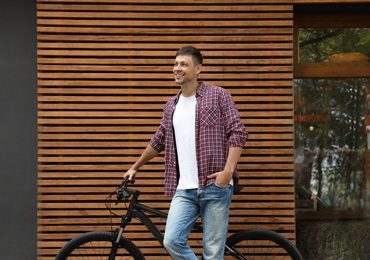 Handsome man with modern bicycle near building outdoors