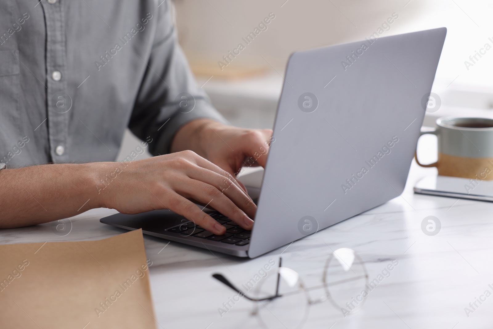 Photo of Man working on laptop at white marble table indoors, closeup