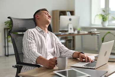 Man with cup of drink snoozing at wooden table in office