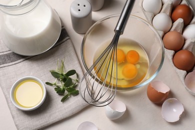 Metal whisk, raw eggs in bowl and ingredients on light table