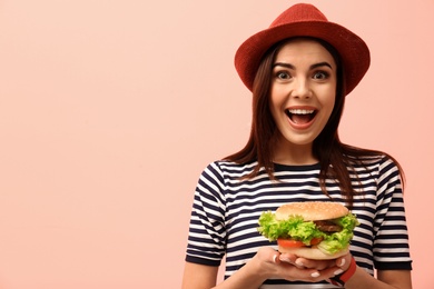 Young woman with tasty burger on color background. Space for text