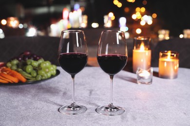 Photo of Glasses of red wine on table against blurred cityscape. Modern outdoor terrace
