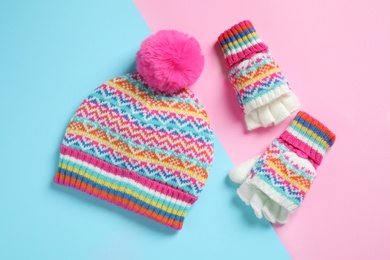 Warm knitted hat and mittens on color background, flat lay