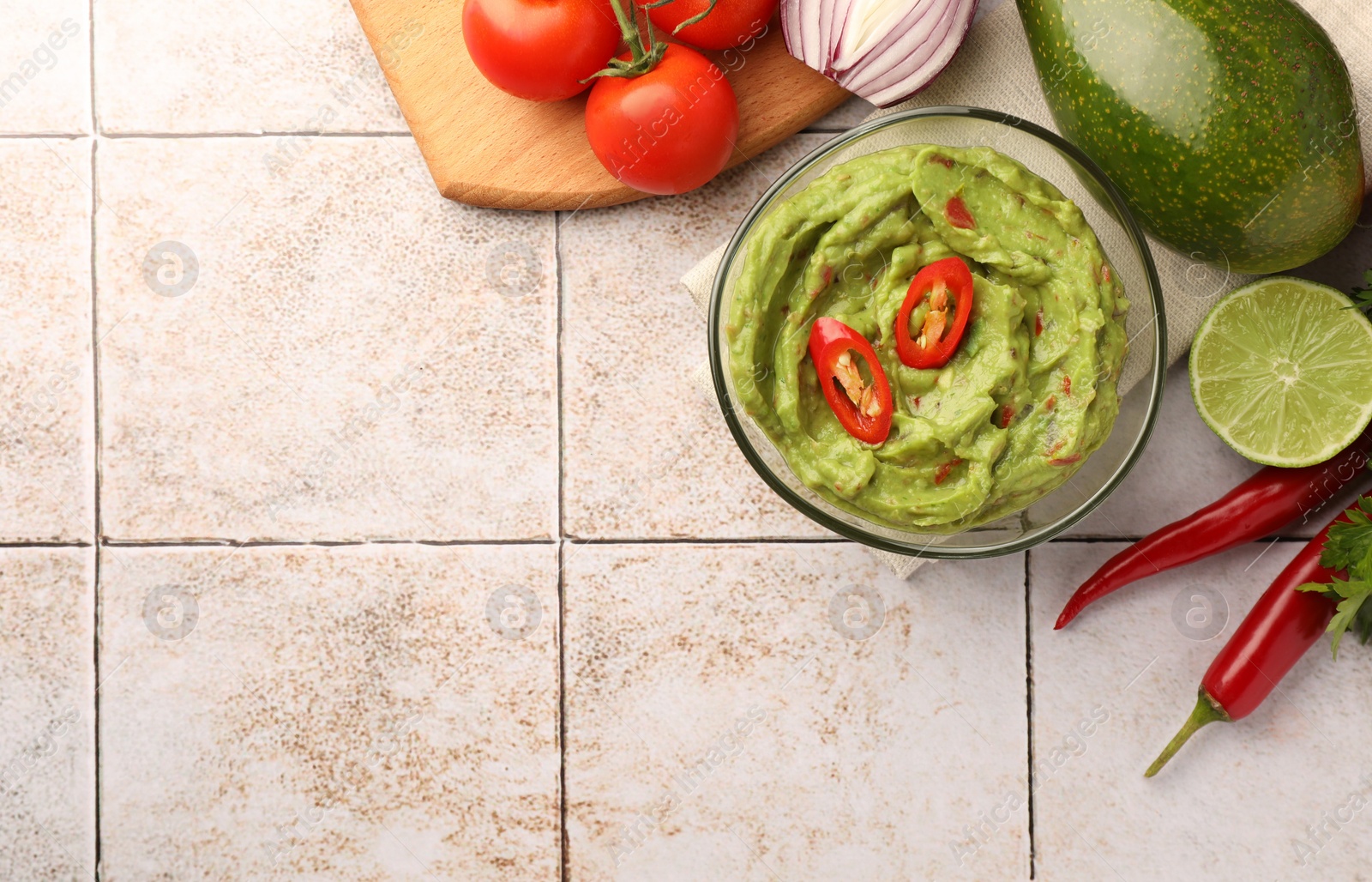 Photo of Bowl of delicious guacamole and ingredients on white tiled table, flat lay. Space for text