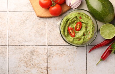 Photo of Bowl of delicious guacamole and ingredients on white tiled table, flat lay. Space for text