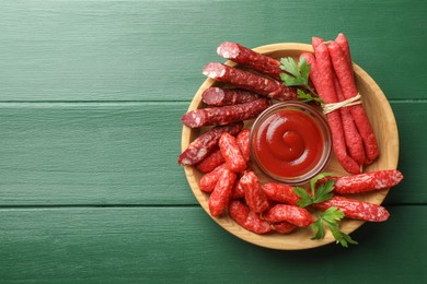 Photo of Different thin dry smoked sausages, parsley and ketchup on green wooden table, top view. Space for text