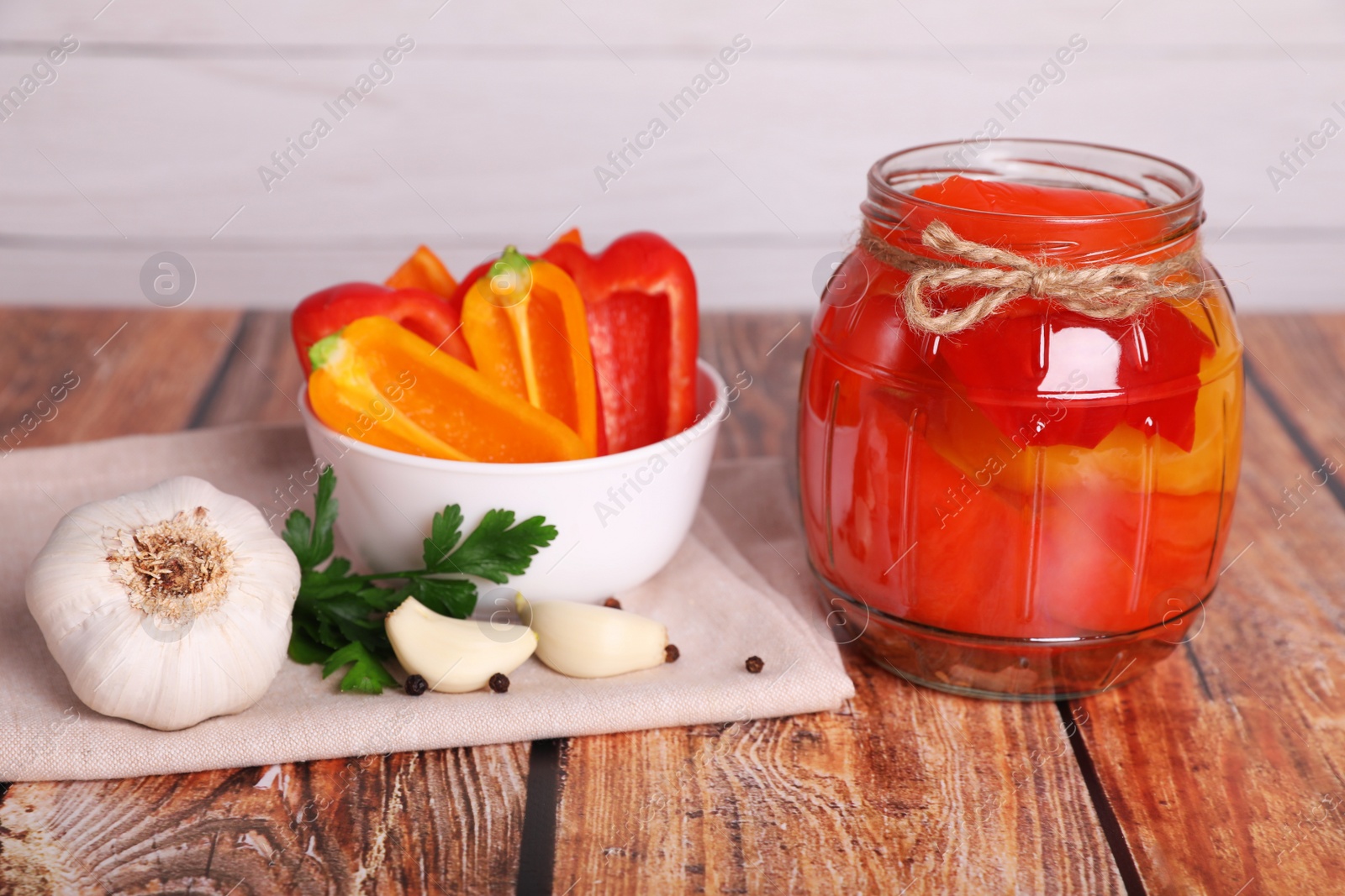 Photo of Jar of pickled bell peppers, parsley, peppercorns and garlic on wooden table