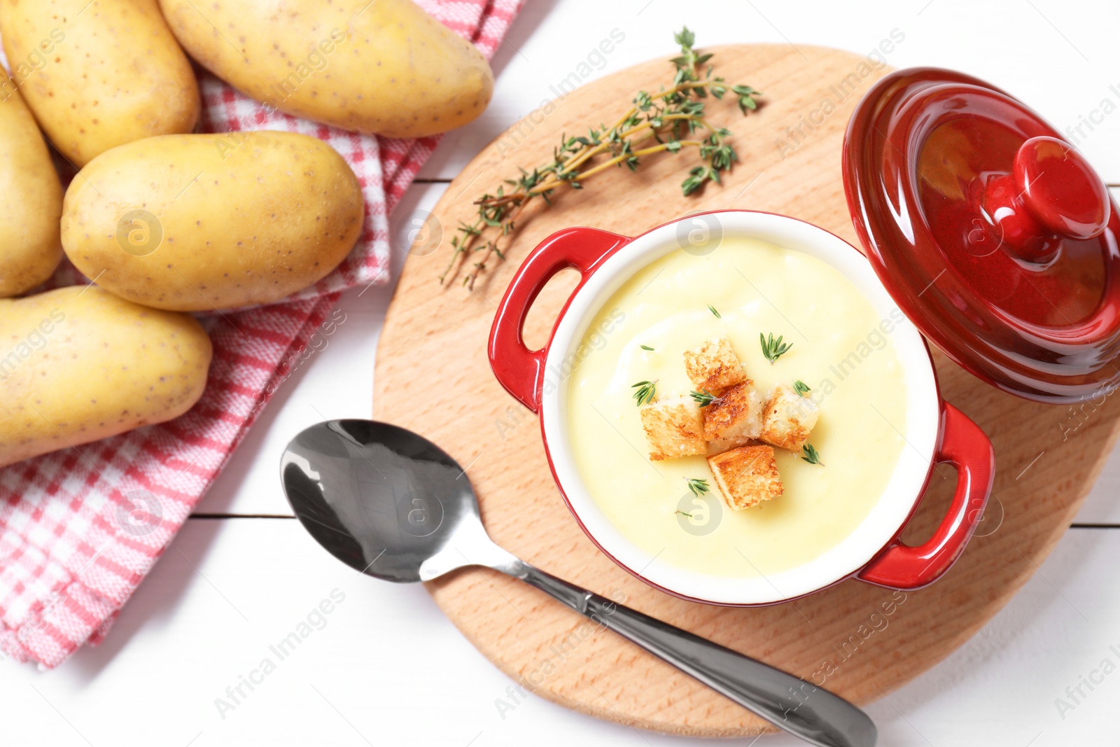 Photo of Tasty potato soup with croutons and rosemary in ceramic pot served on white wooden table, flat lay