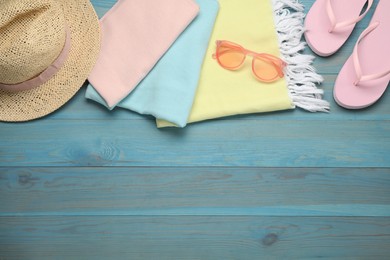 Photo of Beach towel, flip flops, straw hat and sunglasses on light blue wooden background, flat lay. Space for text