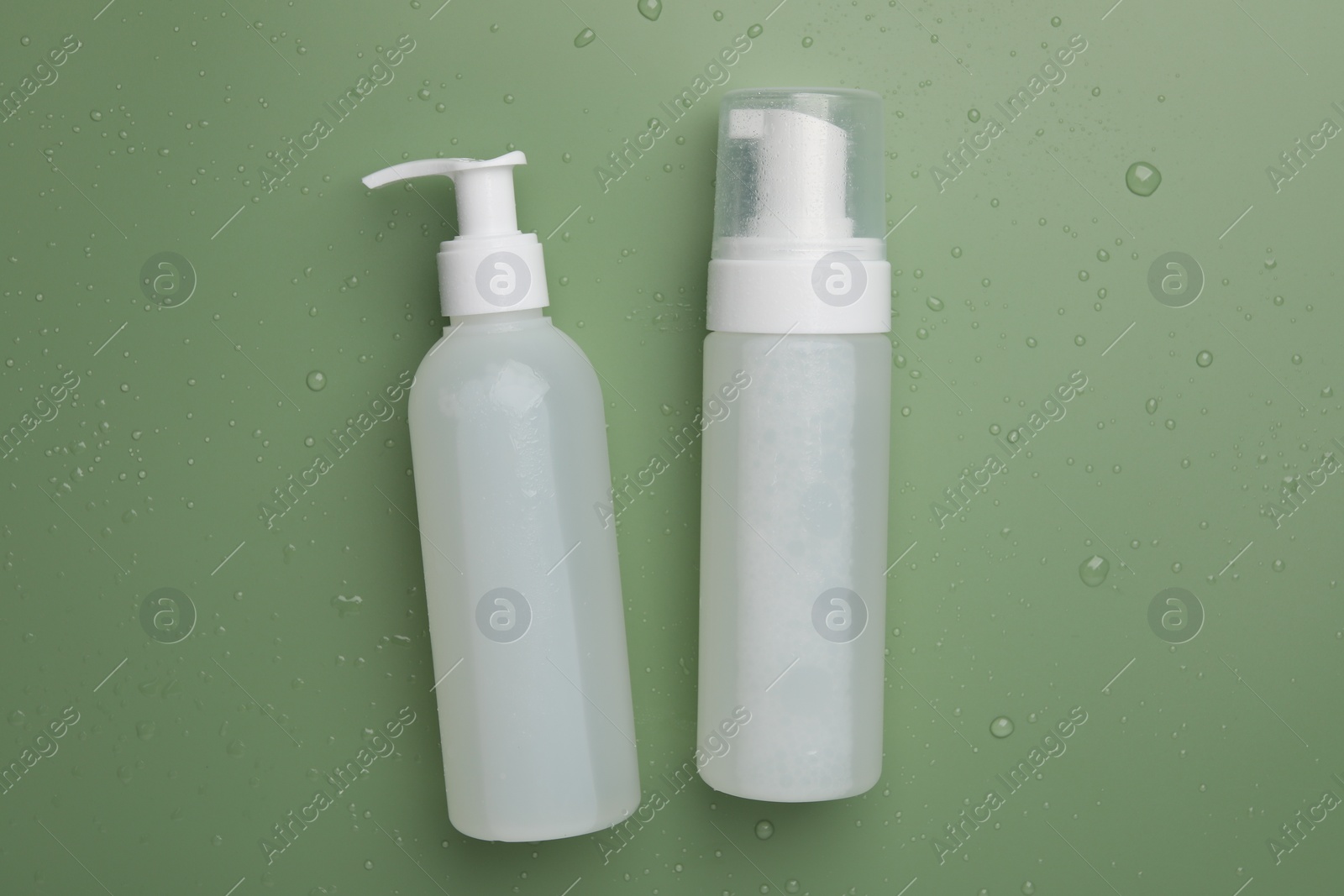 Photo of Wet bottles of face cleansing product on green background, flat lay